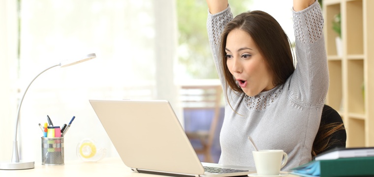 Junge Frau am Computer freut sich über gelungene Bachelorarbeit.