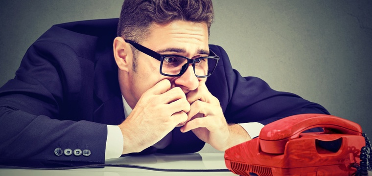 Junger Mann in Business Outfit wartet verzweifelt vor einem Telefon.