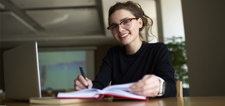 Junge Studentin arbeitet mit Computer und Notizbuch in einem Seminarraum.
