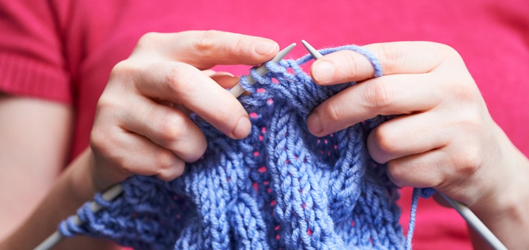 Frauenhände, die einen Schal stricken, in Nahaufnahme.