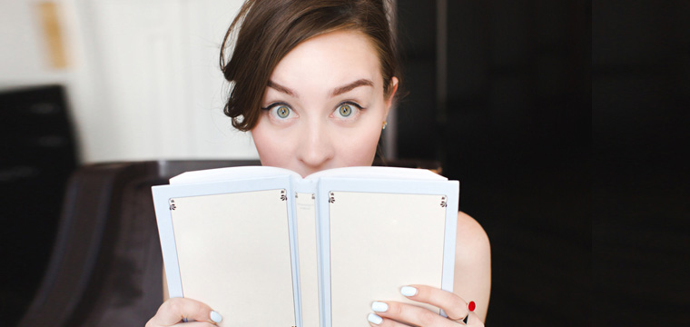 Junge Frau schaut hinter Buch hervor