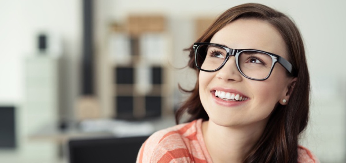 Junge Frau mit Brille blickt zufrieden und lächelnd nach oben.